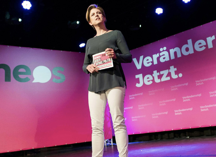 NEOS leader on a stage using a large campaign graphics system